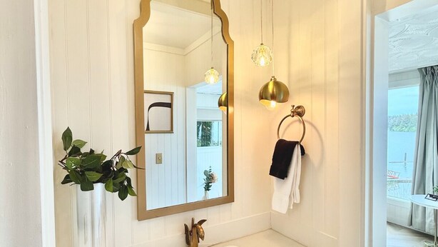 Une salle de bain avec un grand miroir, une plante suspendue, un porte-serviettes et une fenêtre donnant sur un beau paysage.