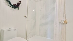 Une salle de bain avec des toilettes, une douche dotée d’une porte en verre et un rideau blanc.