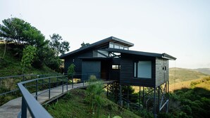A modern house with a wooden exterior, elevated on stilts, and a small deck leading to the entrance.