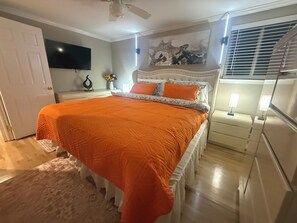 Un dormitorio con una cama grande, ventilador de techo, televisor de pantalla plana, un cuadro y una ventana con persianas.
