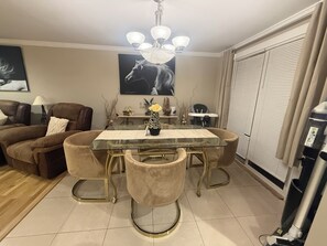 Un comedor con mesa de vidrio, sillas acolchadas, candelabro y un cuadro con tema de caballos en la pared.