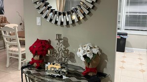 Een kamer met een ronde spiegel aan de muur, een glazen tafel met metalen poten en twee vazen met bloemen.