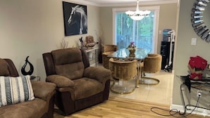 Een woonkamer met een bruine bank, een glazen salontafel en een eethoek met een ronde tafel.
