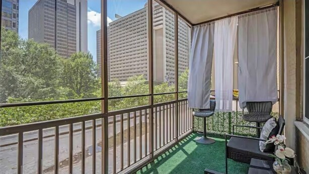 A balcony with a view of tall buildings and greenery.
