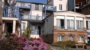 Un immeuble à plusieurs étages doté de balcons, d’un jardin fleuri et d’une enseigne indiquant « Odal Accu ».