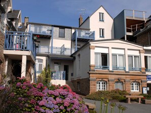 Ein mehrstöckiges Gebäude mit Balkonen, ein Blumengarten im Vordergrund und ein Schild, das ein Hotel oder eine Unterkunft kennzeichnet.
