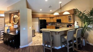 Una cocina moderna con una isla central, taburetes de bar, armarios de madera y un espejo grande.