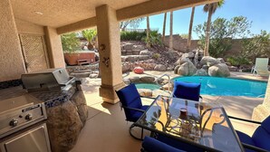 Un patio exterior con una parrilla, zona de estar y piscina.