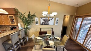 Una cocina moderna con comedor. Incluye una mesa de vidrio, sillas, una planta en maceta y una araña.