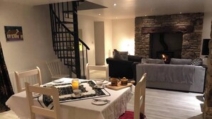 A dining area with a table set for breakfast, a stone fireplace, and a staircase. - Lovingly restored 19th-century Bluestack Mountain farm-cottage hideaway (Letterbarrow)