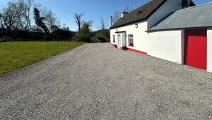 A gravel driveway leading to a white building with red accents and a red door. - Lovingly restored 19th-century Bluestack Mountain farm-cottage hideaway (Letterbarrow)