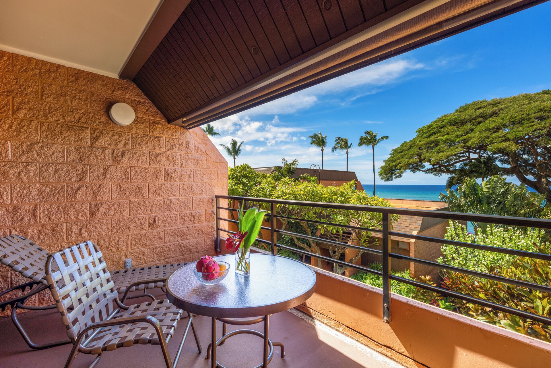 A balcony with a view of the ocean, a round table with a vase of flowers, and two chairs.