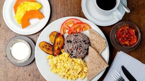 A breakfast plate with scrambled eggs, black rice, fried plantains, tomato slices, toast, and a small bowl of salsa. - Lindora Ranch (Monteverde)