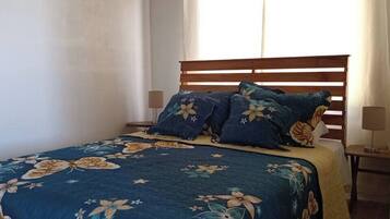 Una cama con colcha y almohadas estampadas, un cabecero de madera y una mesita de noche con lámpara.