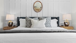 A neatly made bed with a white duvet, a dark headboard, and patterned pillows. There are two bedside tables with lamps and a framed picture above the bed.