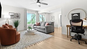 A modern living room with a sofa, a coffee table, a desk with a chair, and a ceiling fan.