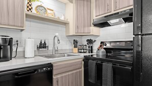 A modern kitchen with light wood cabinets, a black refrigerator, a stainless steel sink, and a stove.