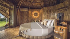 Ein rundes Bett mit Holz-Kopfteil, einem Nachttisch und einer Wandleuchte.