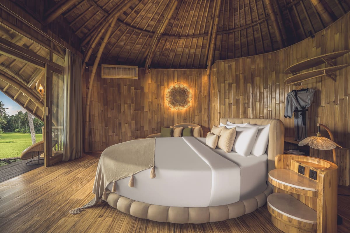 A circular bed with a wooden headboard, a bedside table, and a wall-mounted light fixture.