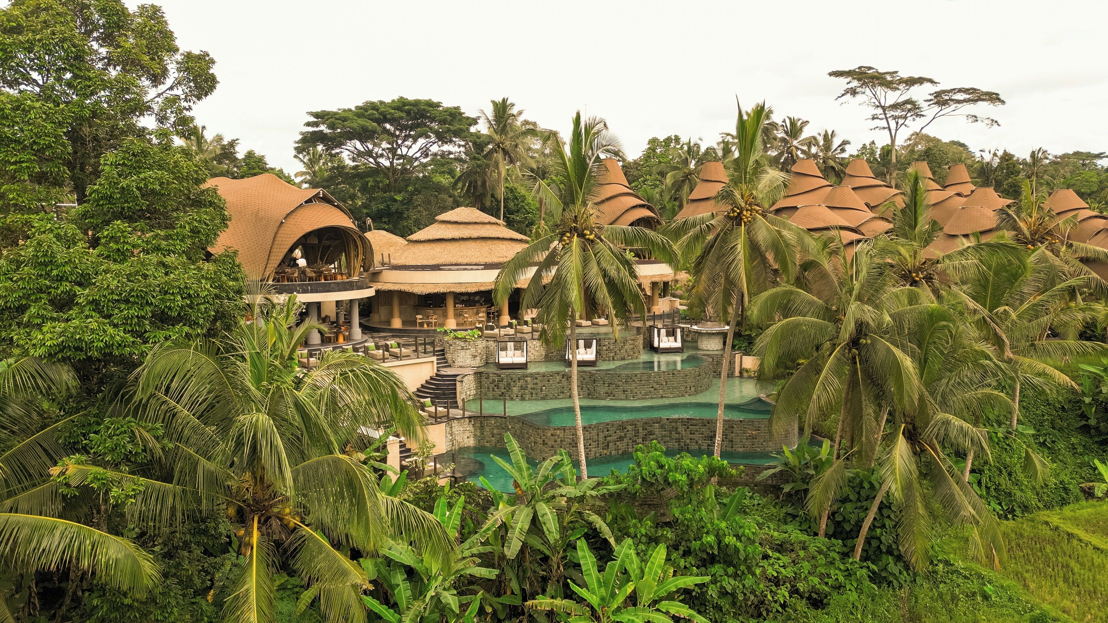Un resort con varias construcciones de techo de paja, una piscina central y abundante vegetación tropical.