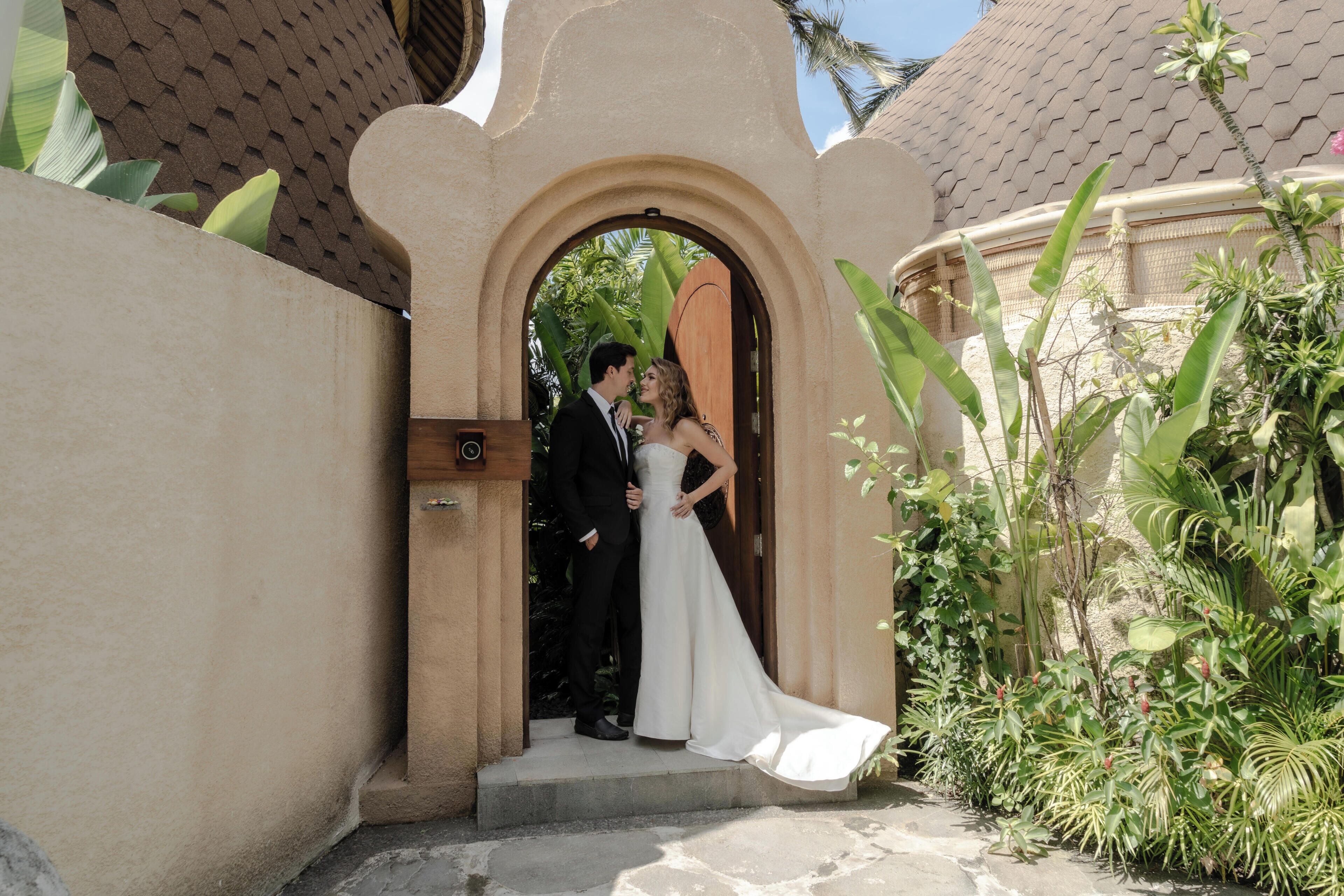 A couple exiting a building with a traditional archway, surrounded by greenery.