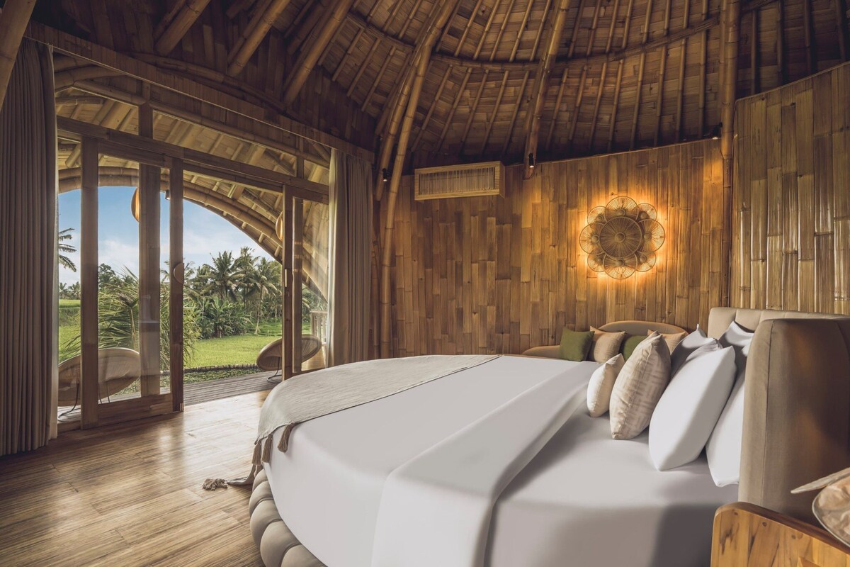 Un dormitorio con una cama grande, paredes de madera y vistas a un paisaje tropical.