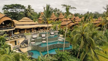 Un complexe hôtelier comprenant plusieurs bâtiments à toits de chaume, un espace piscine central et une végétation tropicale luxuriante.