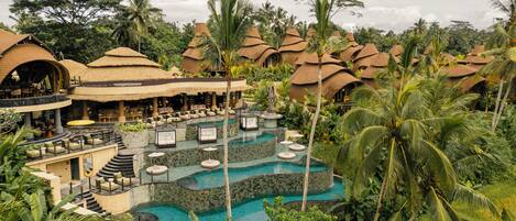 A resort with multiple thatched-roof structures, a central pool area, and lush tropical vegetation.