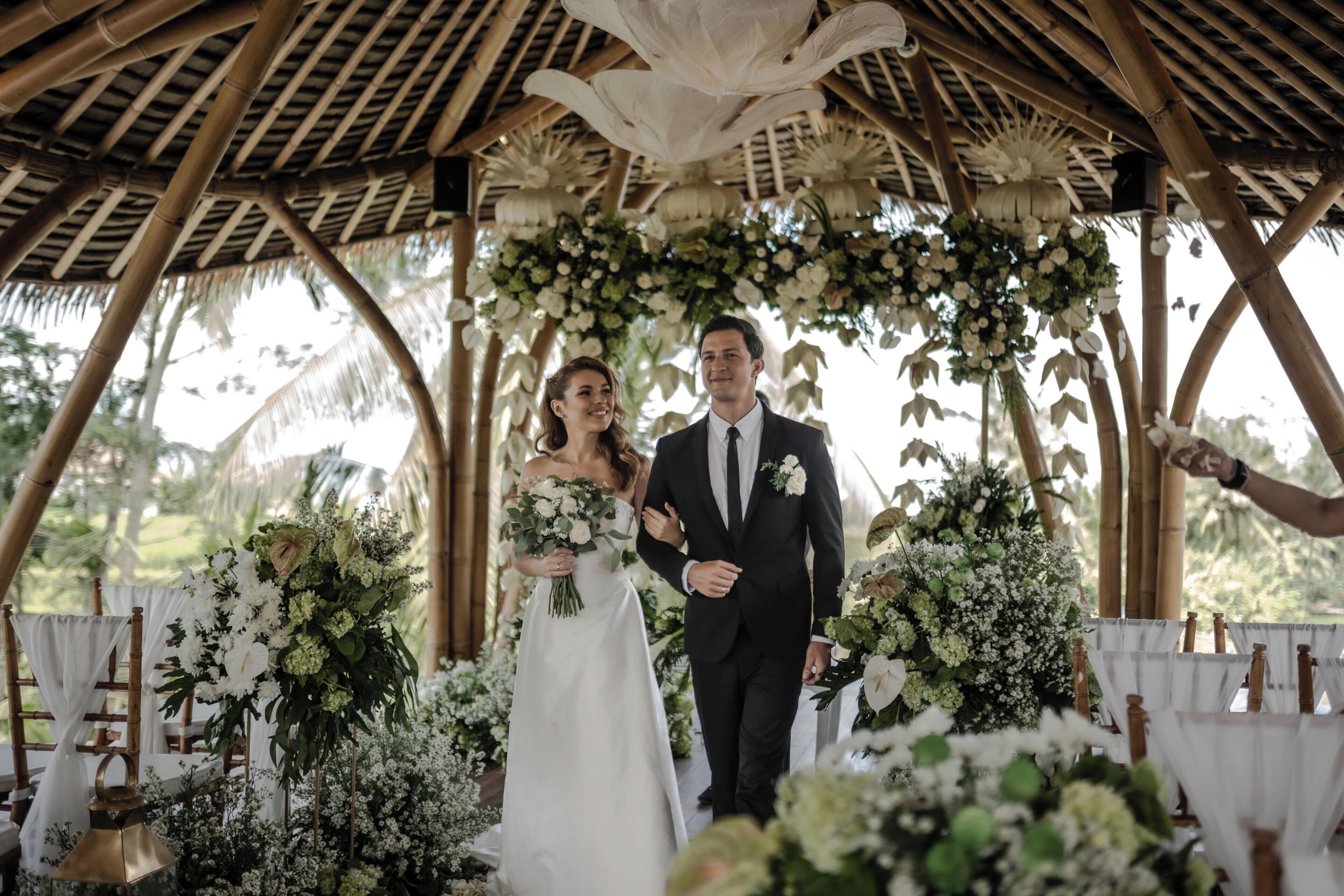 Una pareja caminando bajo una estructura de bambú con decoraciones florales.