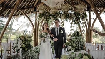 Una pareja caminando bajo una estructura de bambú con decoraciones florales.