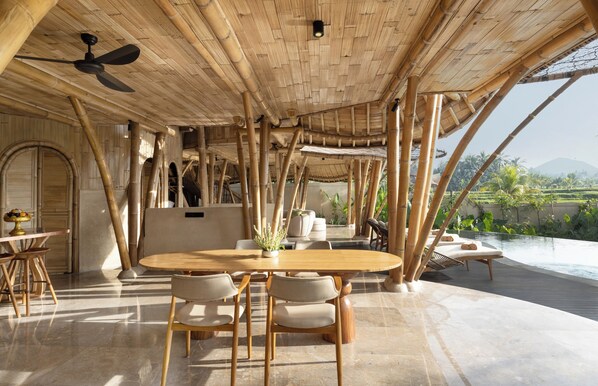 A bamboo-themed interior with a dining area, a ceiling fan, and a view of a pool and greenery.