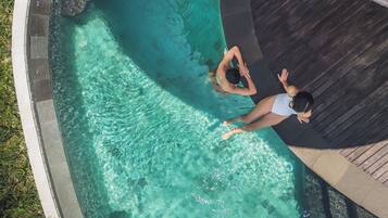 An aerial view of a swimming pool with clear water, a curved edge, and a wooden deck surrounding it.