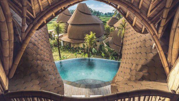Ein Pool mit Blick auf traditionelle Gebäude mit Strohdach und üppigem Grün.