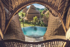 A pool with a view of traditional thatched-roof buildings and lush greenery.