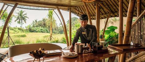 A chef preparing food at a wooden table with a view of a lush green landscape.