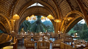 Ein Restaurant mit Bambusdecken, Korbmöbeln und Blick auf Palmen.