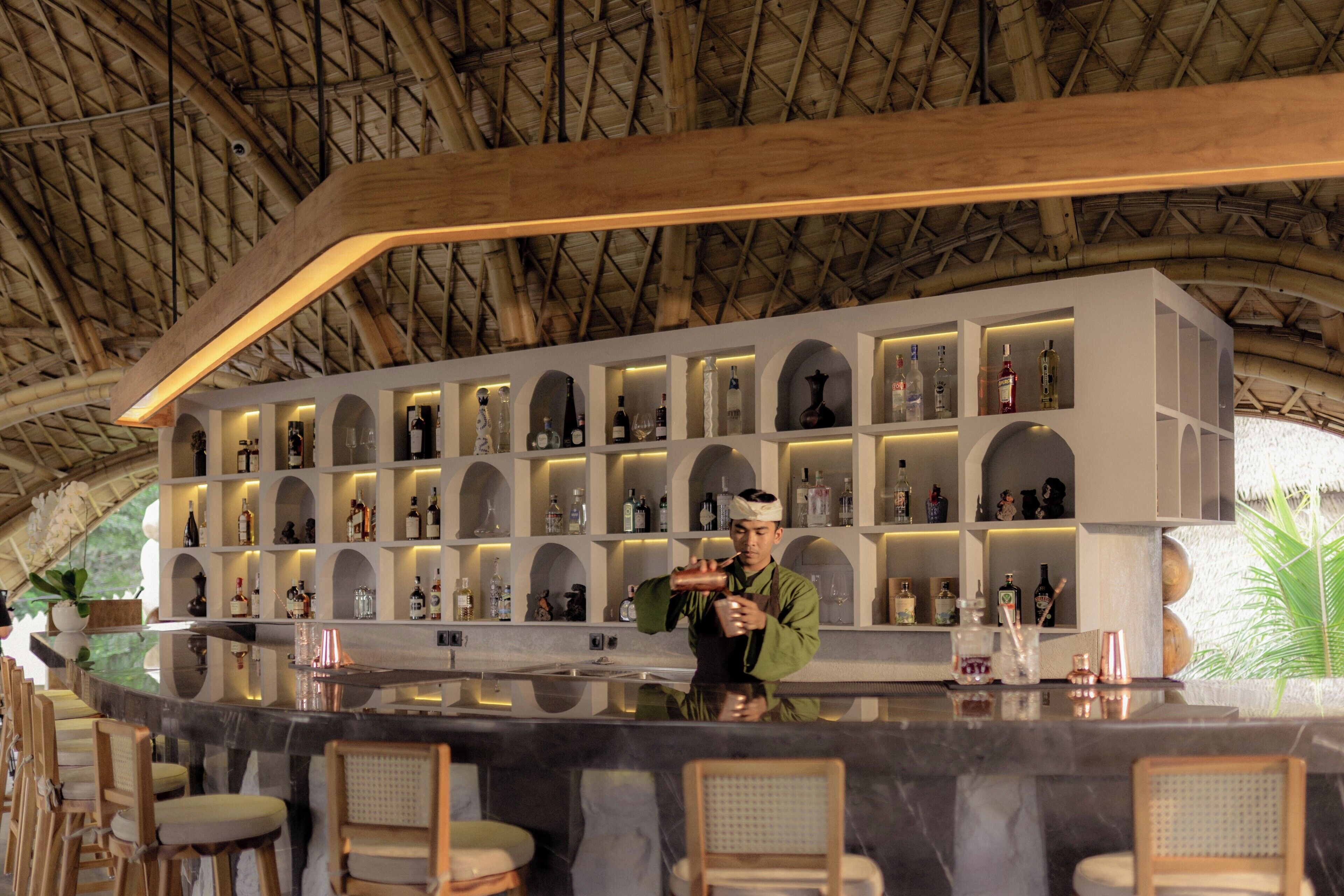A bar area with a bartender, shelves with bottles, and a thatched roof.
