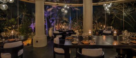 Un comedor interior con mesas redondas, sillas e lámparas colgantes esféricas.