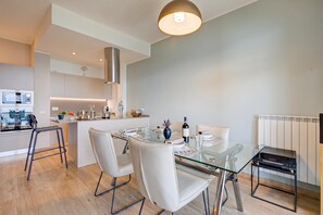 A modern kitchen with a central island, a dining area with a glass table, and a built-in radio.