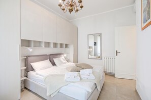 A bedroom with a bed, bedside tables, a mirror, a radiator, and a door.