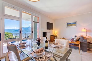 A modern living room with a glass dining table, seating, and a view of the sea.