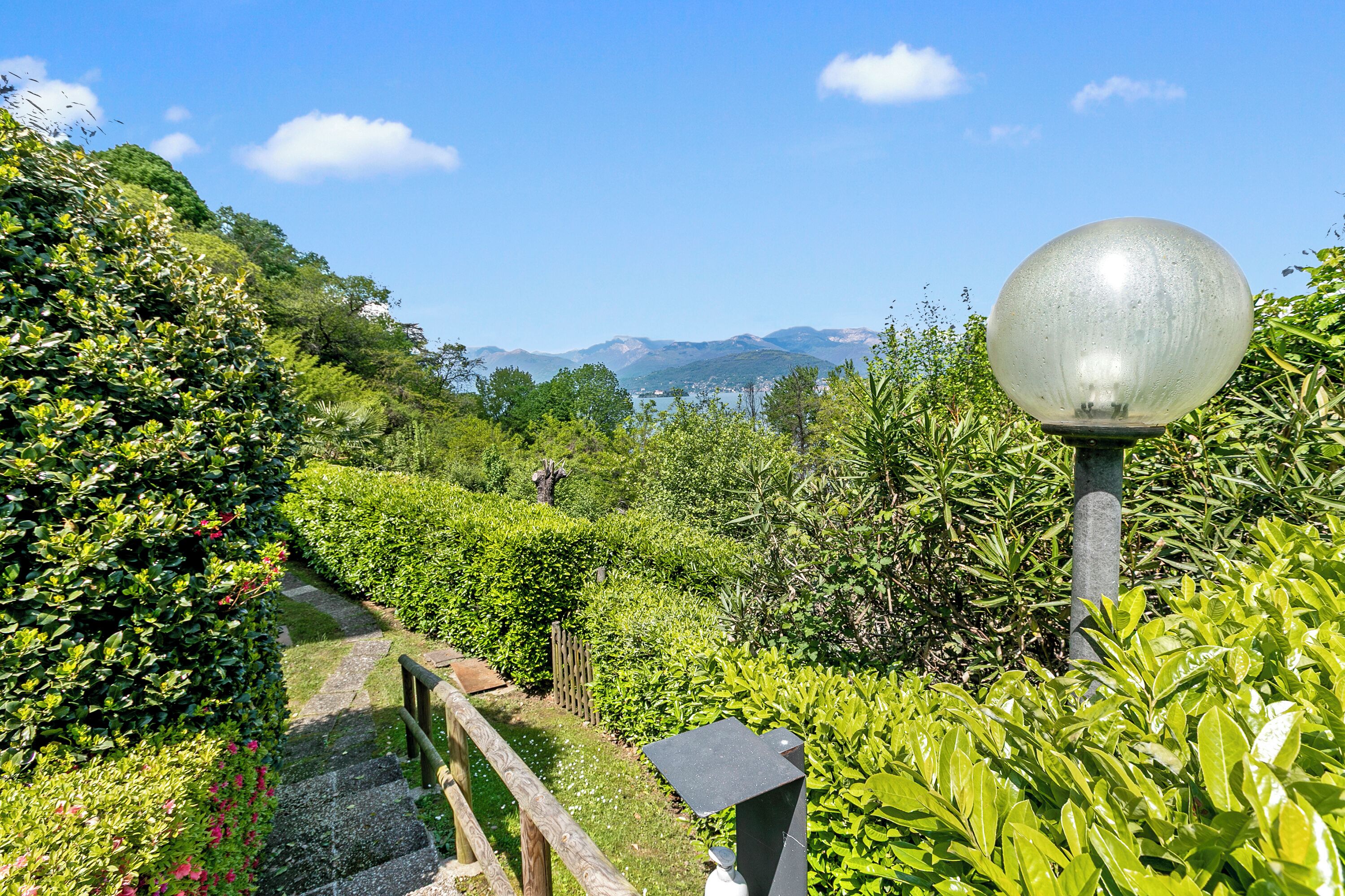 A pathway through a lush garden with a metal lamp post and a stone bench.