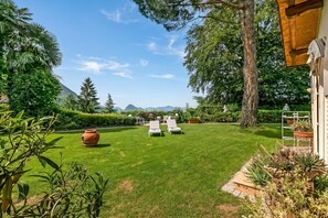 Une pelouse bien entretenue, agrémentée de deux chaises longues blanches, d’un grand arbre et offrant une vue sur des montagnes lointaines.