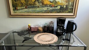 Una mesa de vidrio con un mantel tejido, una cafetera, miel, té y recipientes de azúcar.