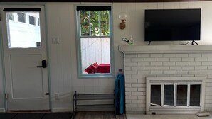 A living room with a white door, a window with a view, a fireplace, and a mounted TV. - Serene Neighborhood Near beach; Under 10 min. to hospitals, universities, & DT (Tacoma)