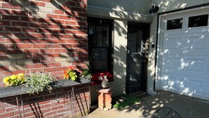 A brick exterior wall, a white garage door, a small planter with flowers, and a tiled outdoor seating area. - Serene Neighborhood Near beach; Under 10 min. to hospitals, universities, & DT (Tacoma)