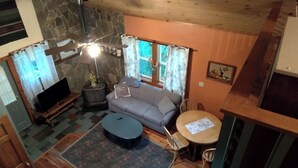 Un salon chaleureux avec une cheminée en pierre, un canapé gris, une table basse ronde et un téléviseur posé sur un meuble en bois.
