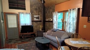 Un salon chaleureux avec une cheminée en pierre, un canapé, une table basse et un coin repas avec des chaises.
