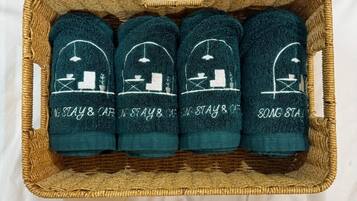 Una cesta de mimbre que contiene cuatro toallas verde oscuro con diseños y texto bordados.