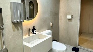 A modern bathroom with a white vanity, a round mirror, a toilet, and a shower area. - song stay (Dangjin)